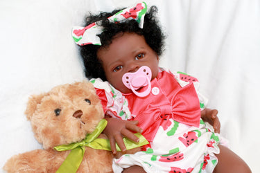 A black baby doll resting peacefully on a white bed, showcasing its soft features and delicate attire.